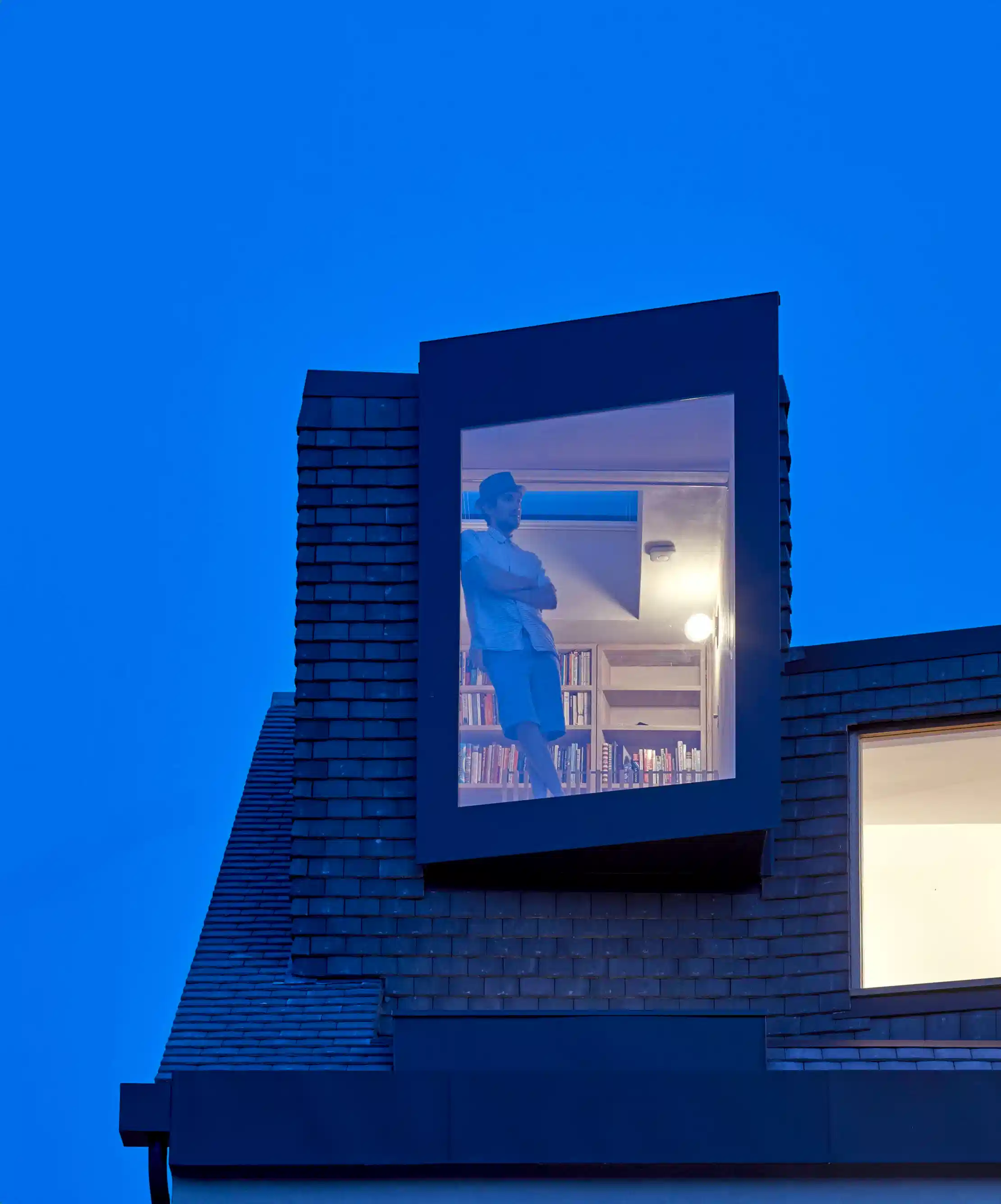 A man watching out of the window from his loft that has been converted into a library. 