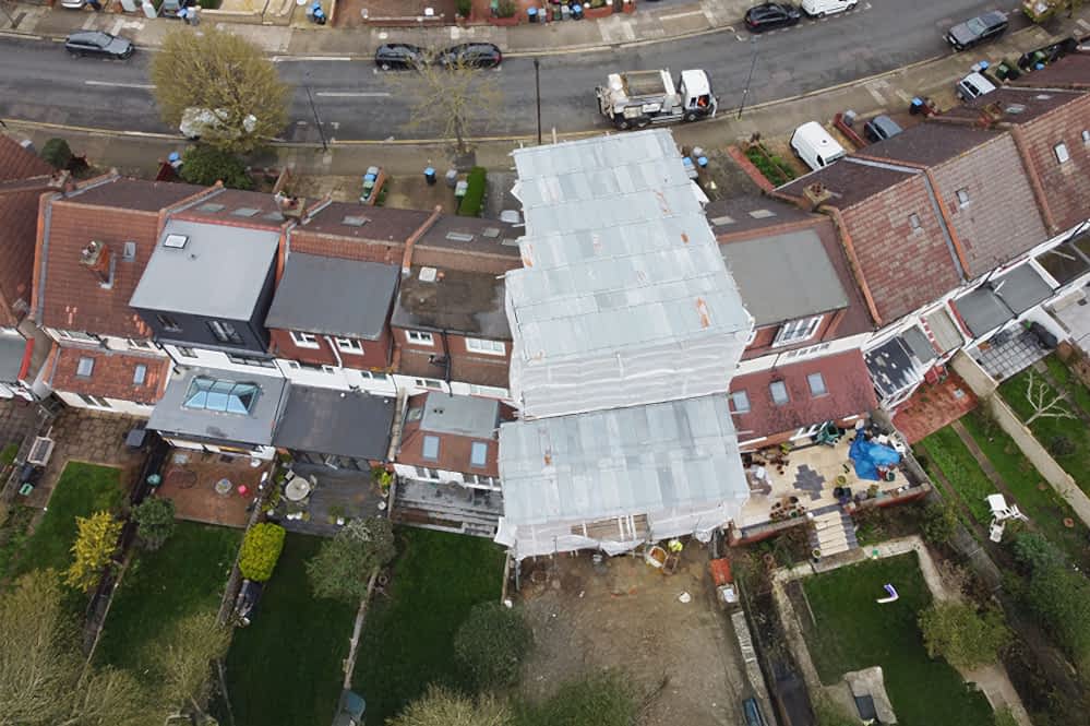 Aerial view of a terraced house undergoing a major renovation, fully covered in scaffolding and protective sheeting, highlighting the scale and care involved in a professional construction project managed by RISE Design Studio.