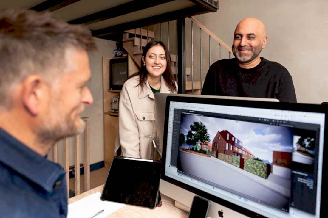 Sean Ronnie Hill and Imran Jahn of RISE Design Studio discussing a sustainable residential project with their team in the studio, with a computer screen showing a 3D design for an energy-efficient London home, reflecting collaboration and low-energy architecture