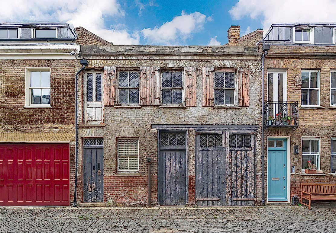 Dilapidated Maida Vale mews house with faded façade and garage door, symbolising the potential of low-energy retrofits to transform London’s historic homes into sustainable dwellings.