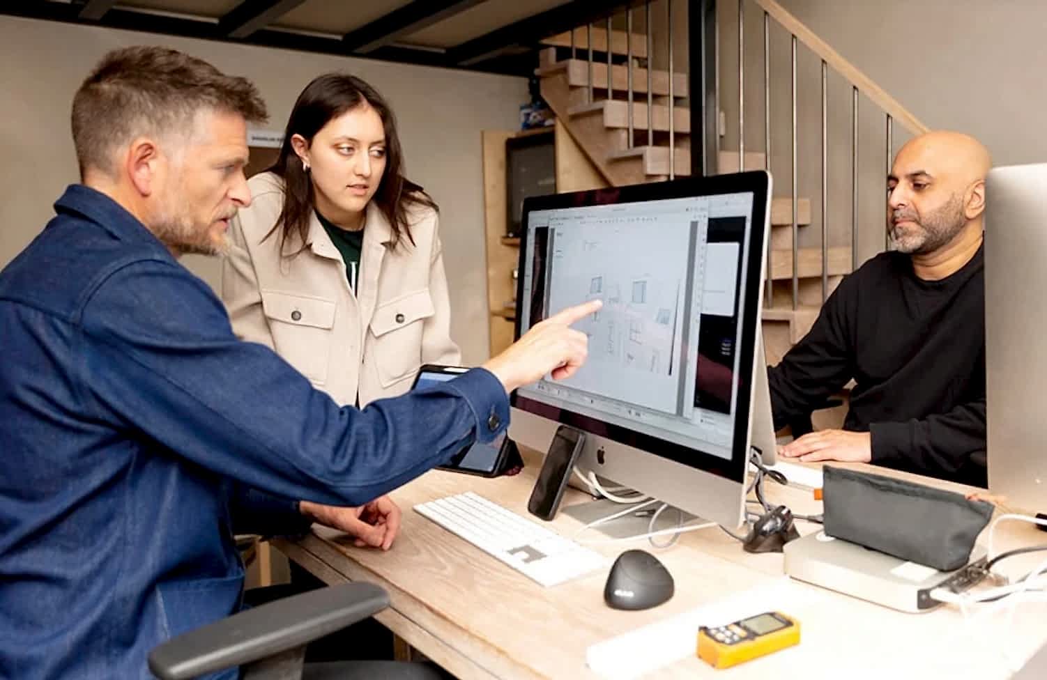 Three architects at RISE Design Studio collaboratively review architectural drawings on screen in a modern studio environment, discussing early-stage planning and sustainable design strategies.