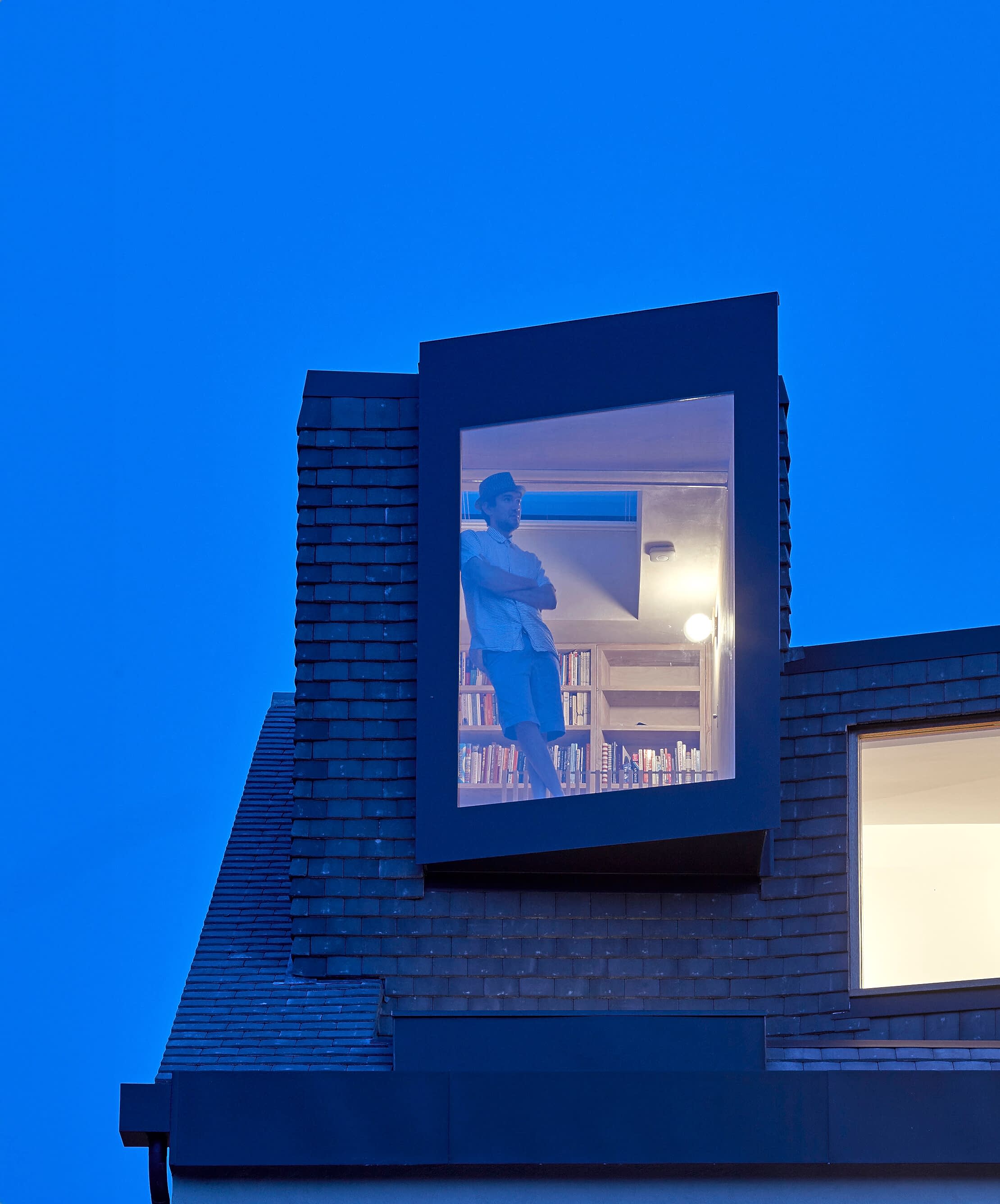 A man watching out of the window from his loft that has been converted into a library. 