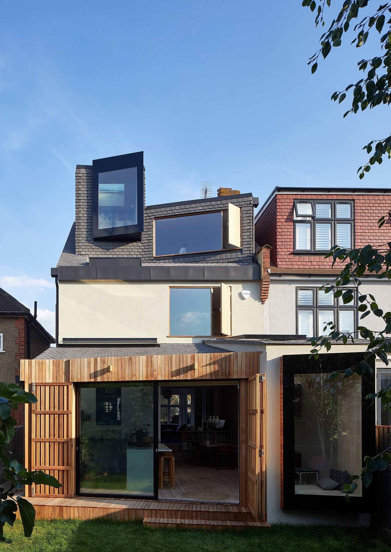 Modern semi-detached house extension featuring a striking loft conversion with angular windows, a timber-clad ground floor addition, and seamless integration of contemporary and traditional design elements.