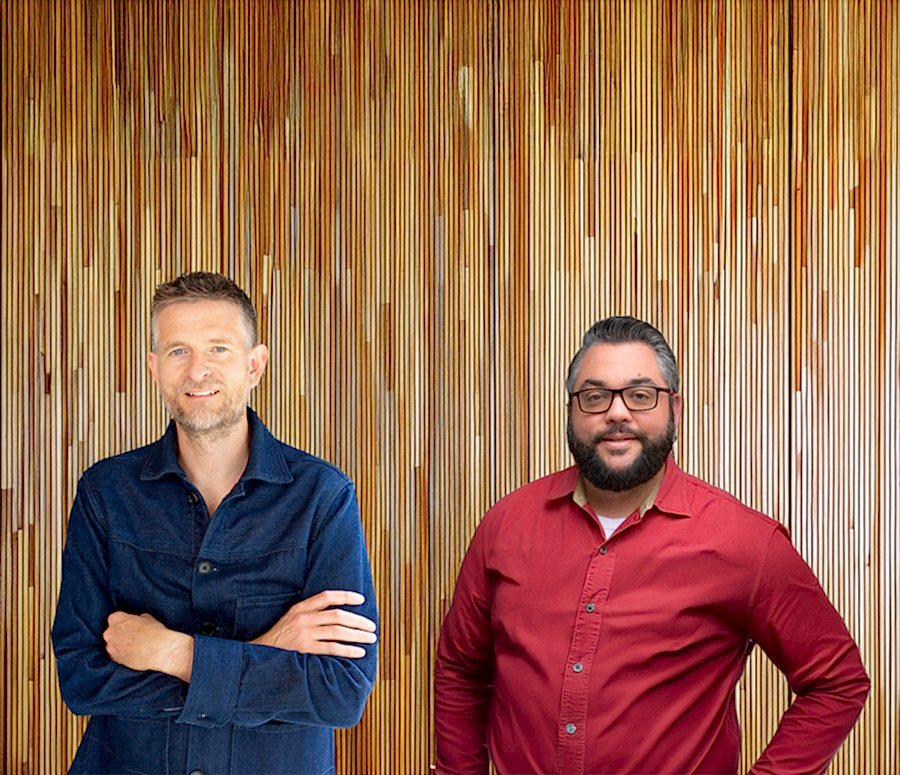 Sean Ronnie Hill, founder of RISE Design Studio, standing alongside Charlie Cicchetti, host of the Green Building Matters podcast, in front of a vertical timber backdrop—capturing their shared commitment to sustainable architecture, natural materials, and regenerative design principles.