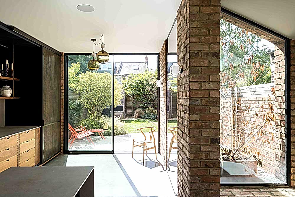 Sustainable rear extension with full-height glazing, reclaimed brick walls, and natural light connecting the indoor living space to the garden, showcasing energy-efficient, low-impact design by RISE Design Studio.